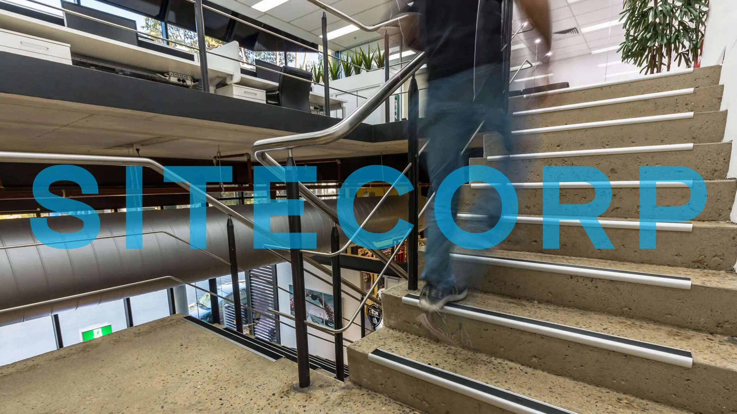 Blurred person ascending stairs with "Sitecorp" text overlay in a modern interior.