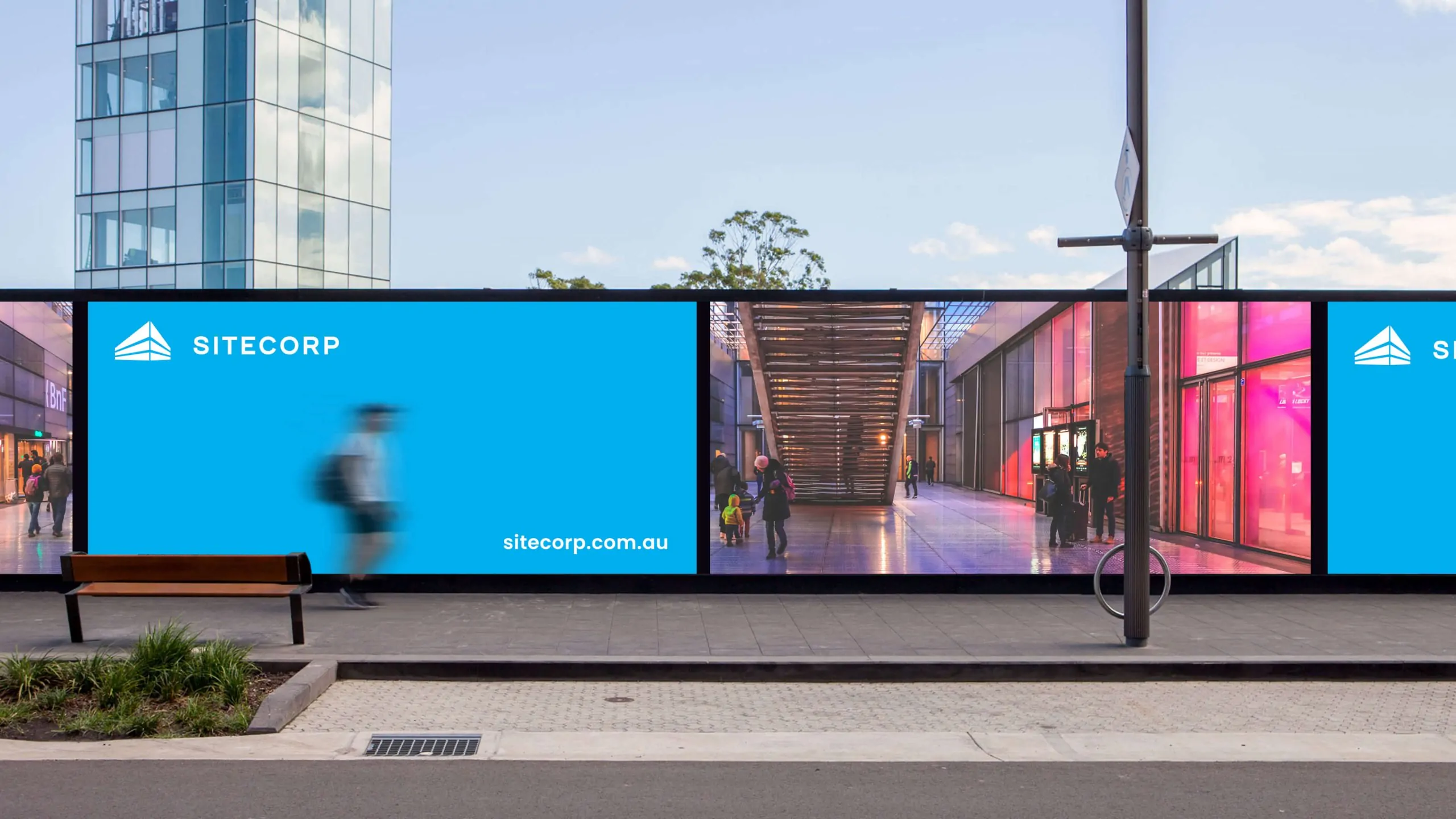 Outdoor advertisement with "Sitecorp" logo, blue background, and modern building image.