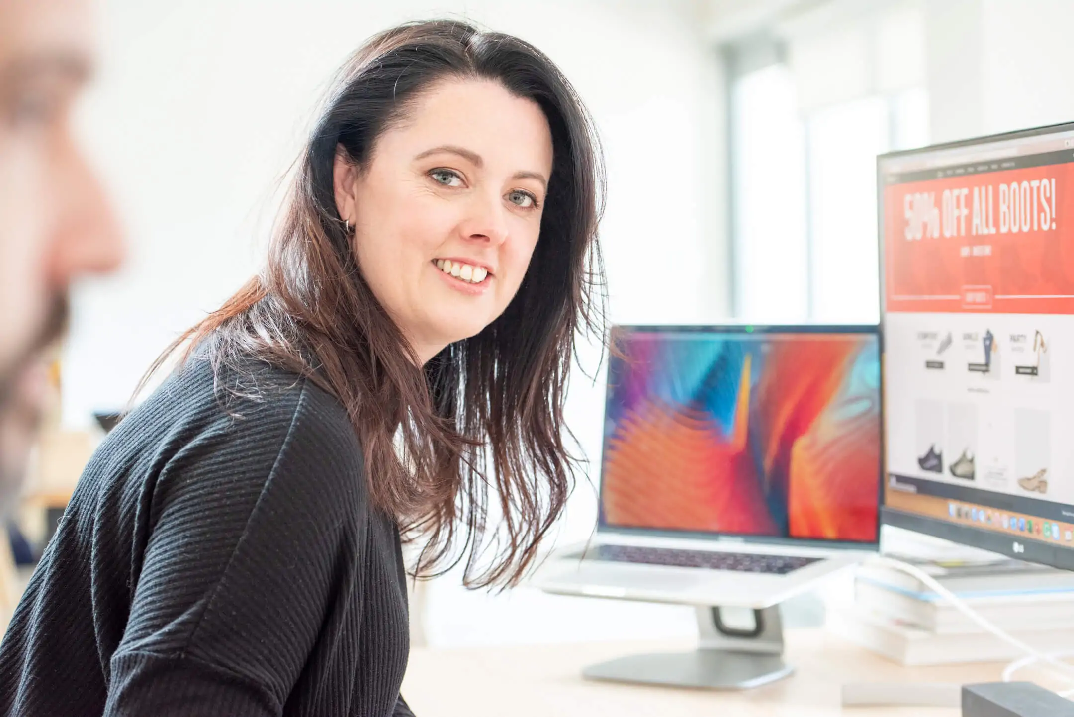 Woman smiling at her desk with computer screens in the background.