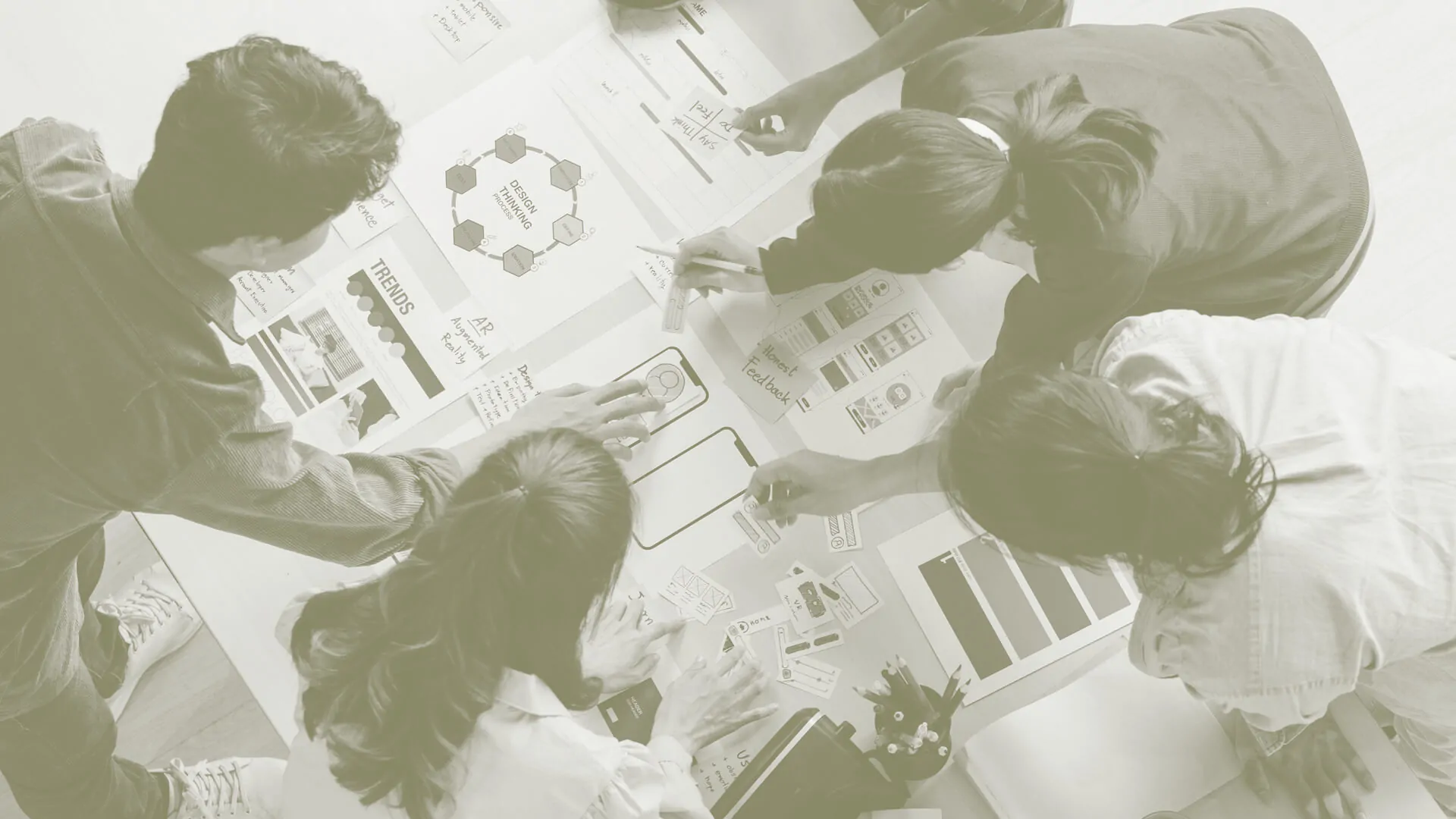 Team collaborating over a table covered with design thinking diagrams and mockups.