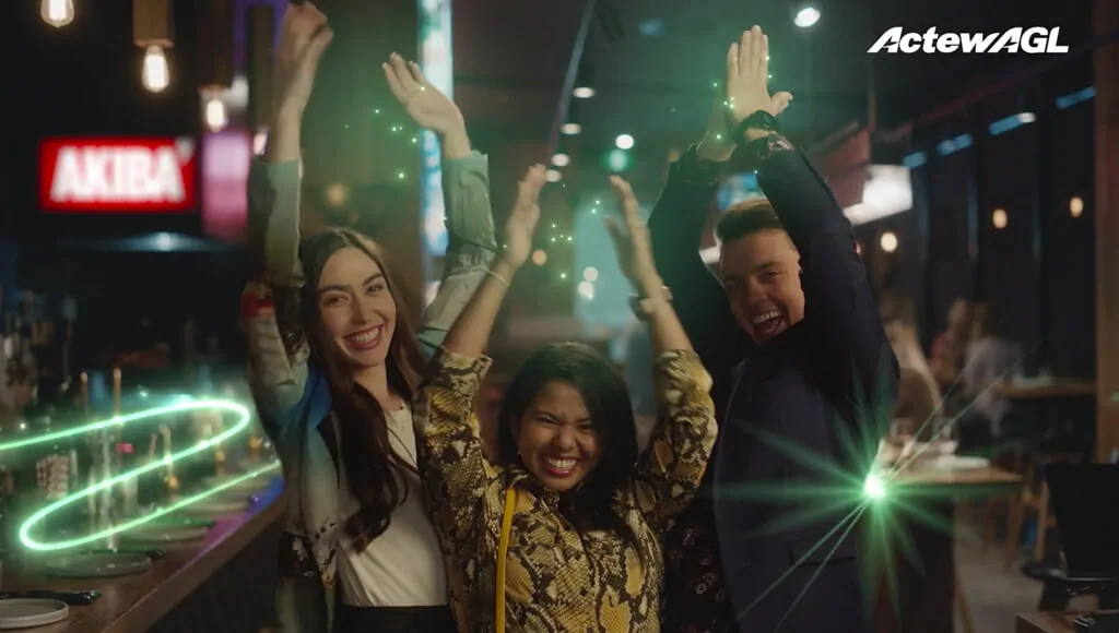 Three people celebrating with glowing green light effects in a lively bar setting.